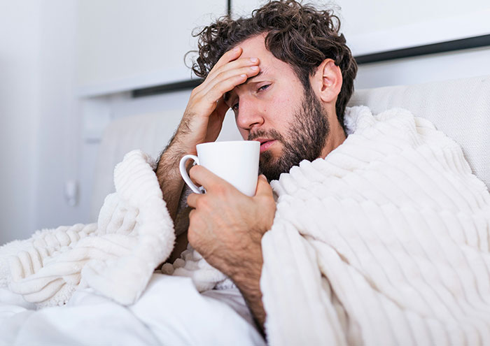 Man wrapped in blanket holding a mug, appearing upset and stressed by seemingly harmless things partners do.