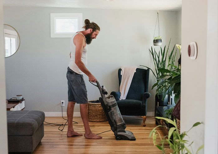 Man vacuuming living room floor barefoot near armchair and plants illustrating seemingly harmless things partners do.