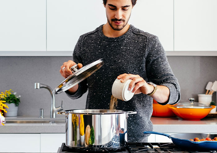 Man pouring ingredients into a pot while cooking in kitchen, illustrating seemingly harmless things partners do.
