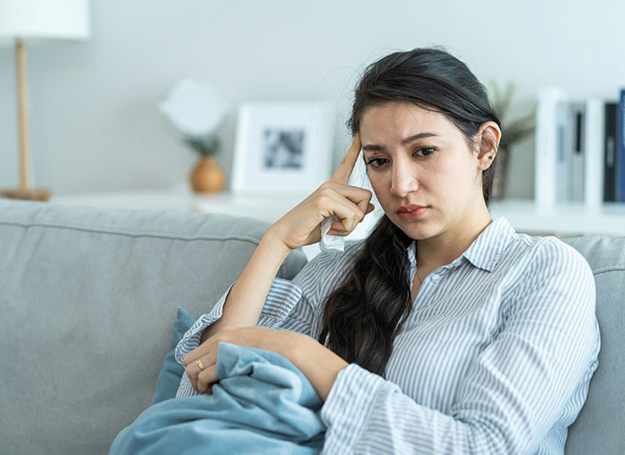 Woman sitting on a couch looking frustrated and thoughtful, illustrating partner behaviors that drive people insane.