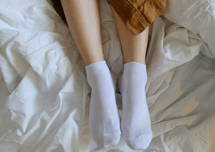 Feet wearing white socks on a rumpled bed sheet depicting seemingly harmless things partners do that drive people insane.