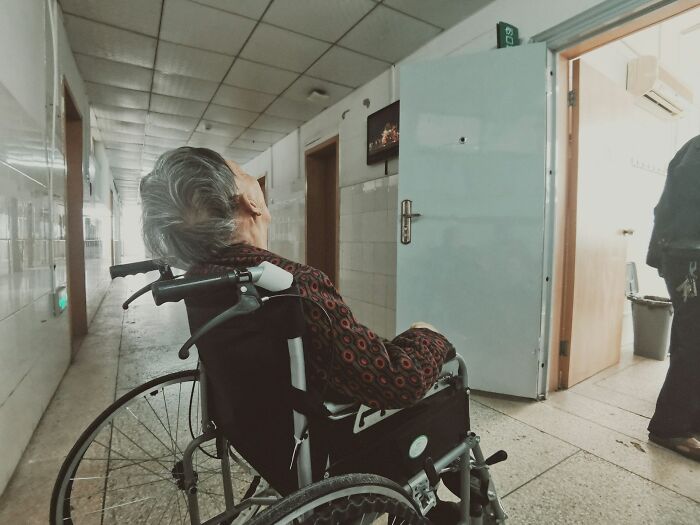 Elderly person sitting in a wheelchair in a hospital hallway, highlighting body design and evolution concerns.