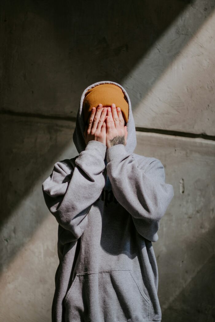 Person in a gray hoodie and mustard beanie covering their face, illustrating emotion behind powerful comebacks.
