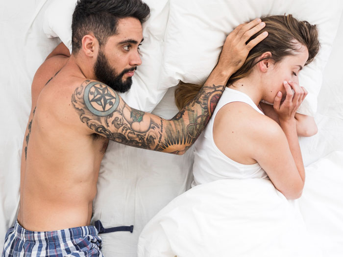 Wife upset in bed next to shirtless tattooed husband, sensing something happened after hearing moaning sounds.