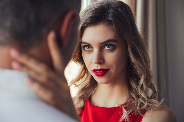 Woman in red dress looking intently at shirtless man, hinting at a complex emotional moment after hearing moaning sounds.