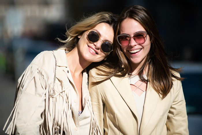 Two women smiling outdoors wearing sunglasses, capturing a candid moment with a close bestie vibe.