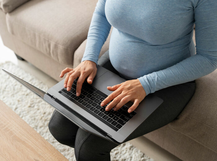 Mulher grávida trabalhando em laptop em casa, representando negação de solicitação de trabalho em casa e processo legal relacionado.