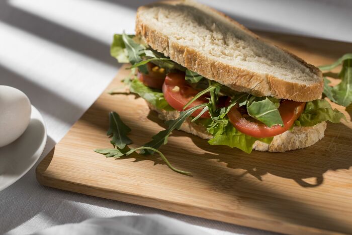 Sandwich with fresh lettuce and tomato on rustic bread placed on a wooden cutting board in natural light.