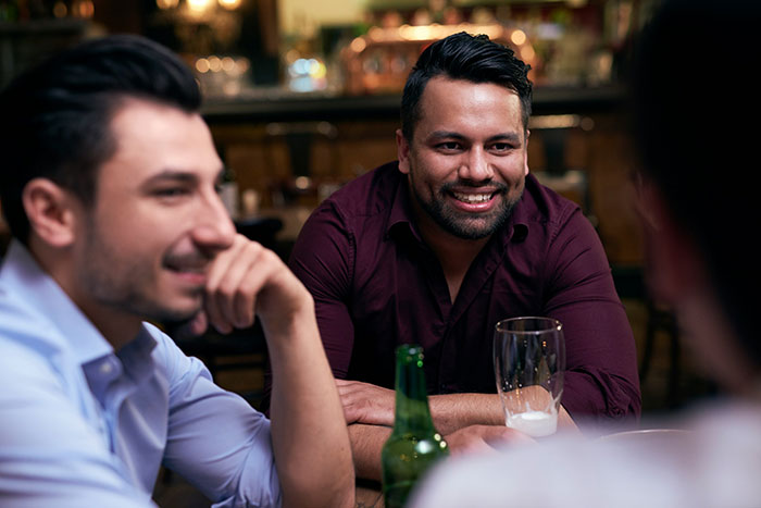 Man smiling and chatting with friends at a bar during a casual evening, referencing guy thinking he imagined ex now living as a man.