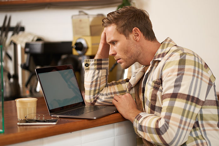Young man in plaid shirt looking at laptop, reflecting on a random meeting revealing his teenage ex now lives as a man.
