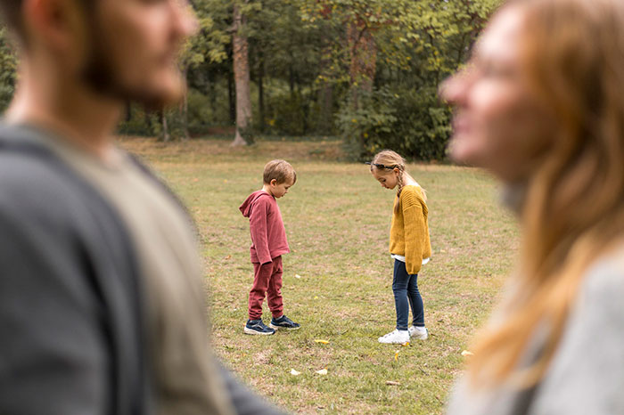 Man and woman blurred in foreground, two children standing apart on grass, reflecting on a random meeting and identity.