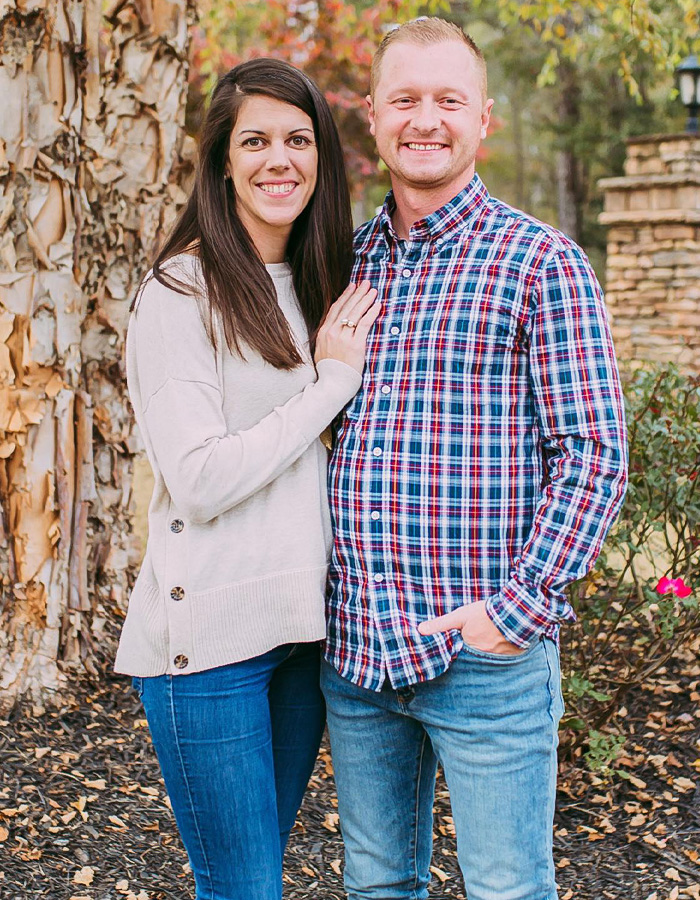 Couple standing outside a home surrounded by autumn foliage, representing teacher's tragic incident after a prank.