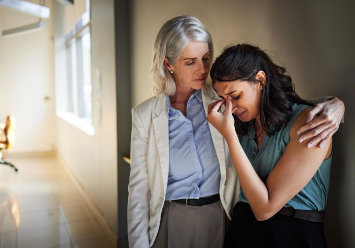 Older woman consoling a younger coworker who is crying in a hallway, showing support during a difficult divorce situation.