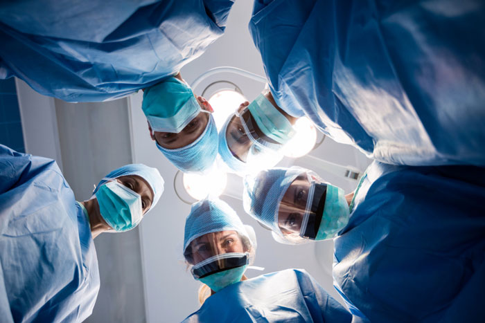 Surgical team in blue scrubs and masks performing an operation under bright operating room lights.