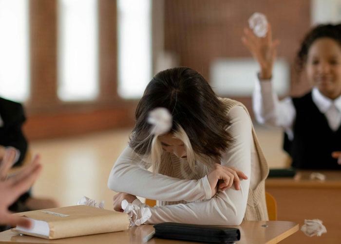 Young woman upset at desk as crumpled papers are thrown, illustrating betrayal and affairs affecting her life.