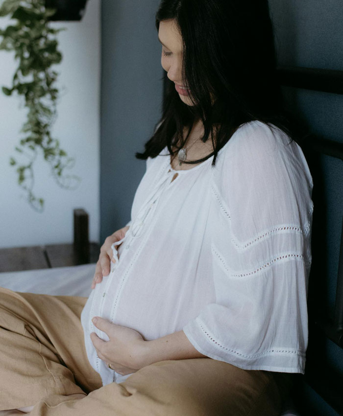 Pregnant woman in white blouse sitting quietly, reflecting on life changes after uncovering husband's affair.