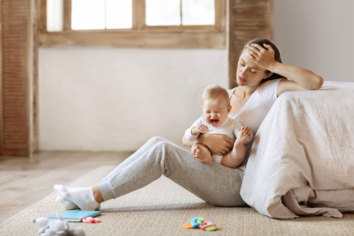 Tired woman holding crying baby, showing emotional stress linked to mental health struggles in a difficult marriage.