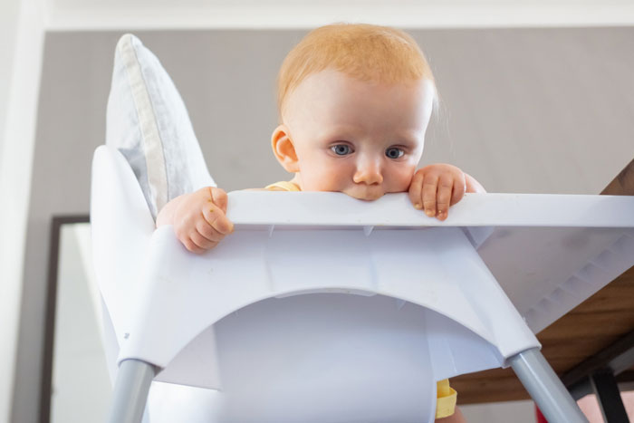 Baby sitting in high chair looking down with curiosity, symbolizing mental health struggles pushing wife to the edge.