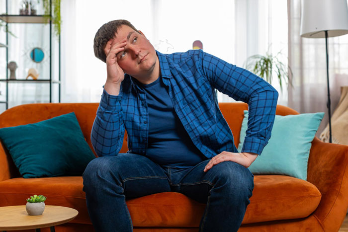 Man sitting on couch looking distressed, illustrating mental health struggles impacting relationship tensions.
