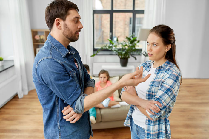 Man telling his best friend to divorce his wife while she looks upset and children sit on a couch in the background