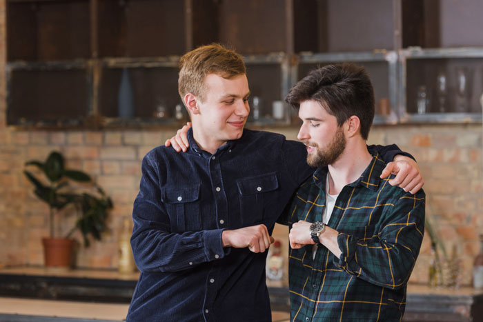 Two men fist bumping in a kitchen with one man subtly sabotaging his best friend's marriage advice.