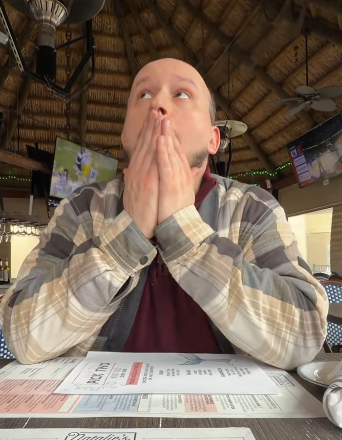 Man in plaid shirt looking shocked at restaurant, capturing moment husband realizes woman he messaged on Tinder is his wife