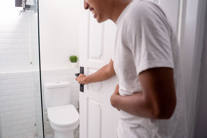 Man opening bathroom door, holding stomach, showing bathroom habit used to avoid parenting duties at home.