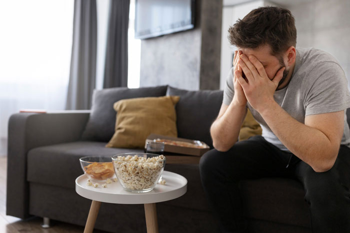 A stressed man sitting on a couch covering his face, illustrating a delusional guy and breadwinner conflict.