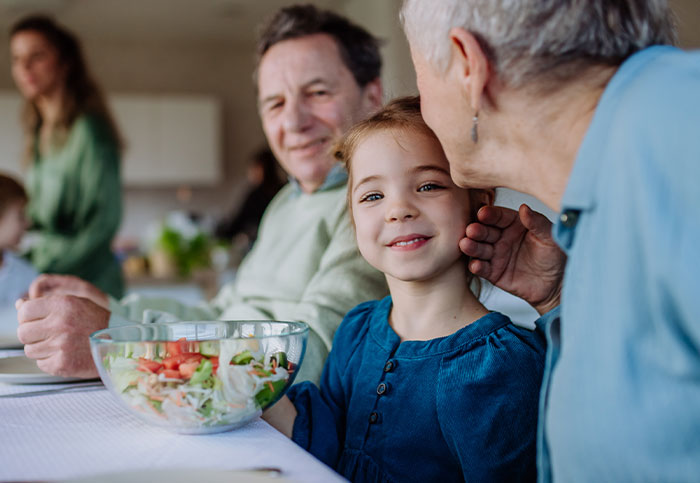 A família compartilha um momento na mesa de jantar enquanto a mulher se muda com a família para fugir dos sogros e de seu acompanhamento planejado.