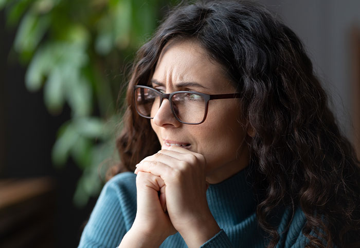 Mulher de óculos parecendo preocupada e pensativa, simbolizando a mudança da família para fugir da situação dos sogros.