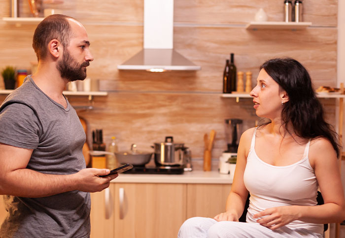 Mulher e marido na cozinha discutindo a mudança da família para fugir dos sogros que os seguem apesar do plano.