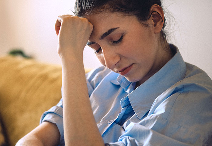 Mulher parecendo preocupada e estressada enquanto está sentada dentro de casa, refletindo conflitos familiares e desafios com sogros.