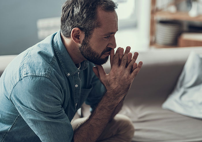 Homem pensando profundamente, sentado em um sofá, refletindo sobre a mudança da família para fugir dos sogros e o acompanhamento planejado.