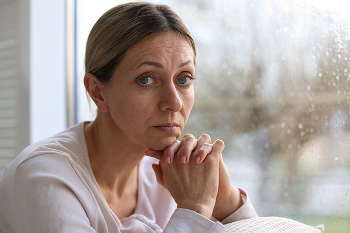 Worried woman sitting by a rainy window, reflecting on a good deed involving a pregnant coworker and consequences.