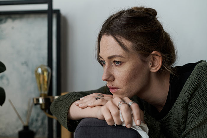 Woman in green sweater looking thoughtful and concerned indoors, reflecting on coworker and pregnancy situation.