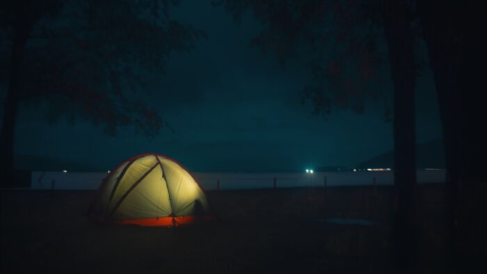 Glowing tent set up at night near a dark forest, illustrating scary camping and hiking stories in a remote location.