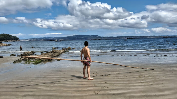 A person holding a cool stick on a sandy beach near the water under a partly cloudy sky.