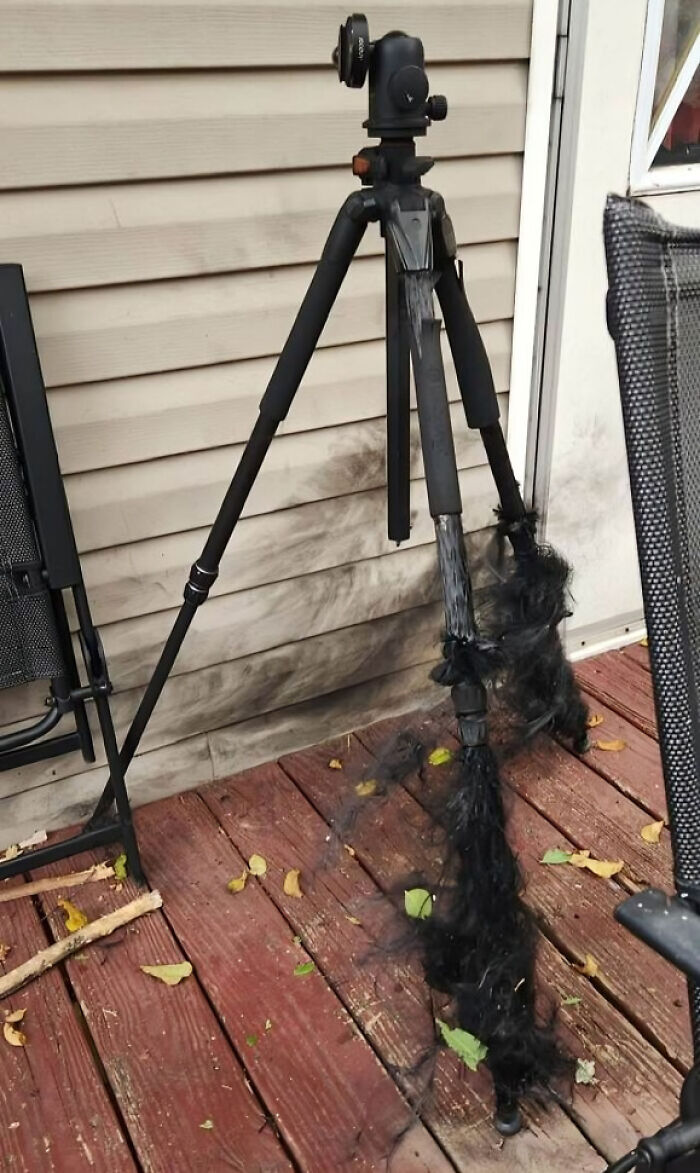 Tripod legs covered in dark soot with black smoke marks on wooden deck and house siding outdoors, showing unreal photos reality.