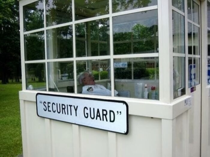 Sign with suspicious quotation marks around security guard outside a small guard booth with a sleeping man inside.