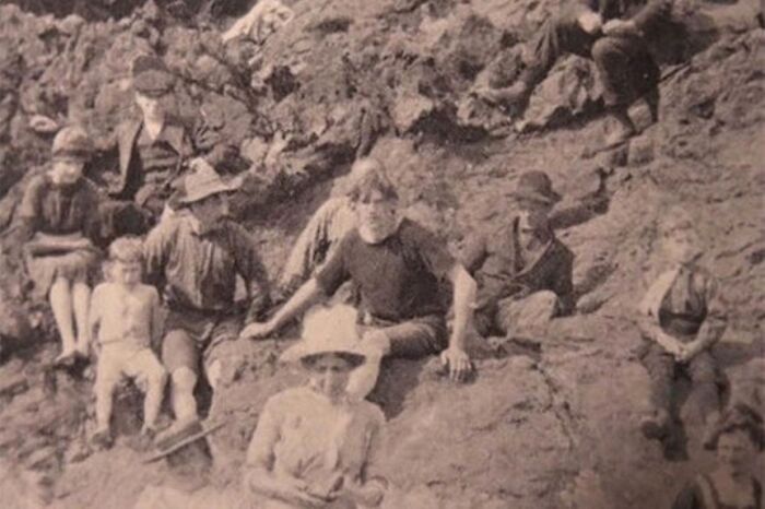 Group of people in an old photograph sitting on rocks, showing strange details that spark time travel theories.