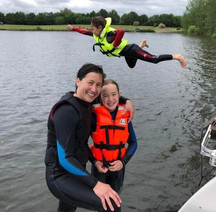 Three people in life vests posing by the water with a child mid-air in a creative and hilarious pose.