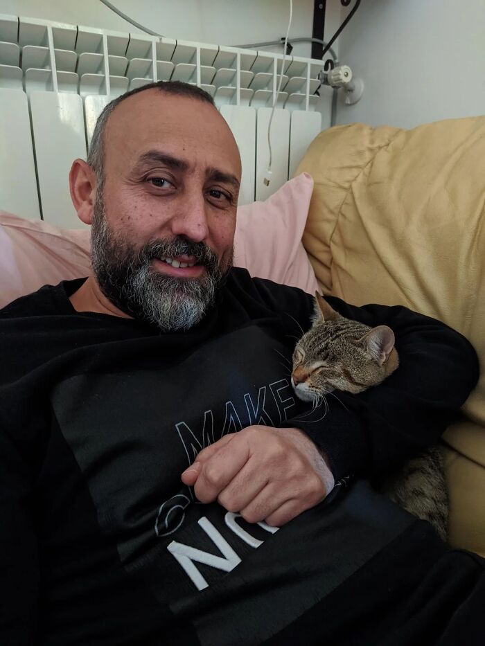 Man cuddling a cat on a couch, showing the bond between dads and the pets they never wanted but now love.