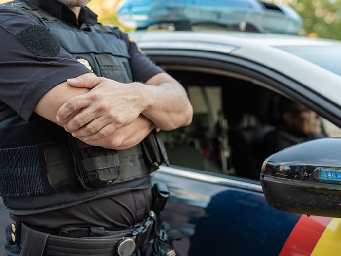ICE officer standing with arms crossed next to police car in a parking lot during a detention incident involving a woman speaking a foreign language ICE officer standing with arms crossed next to police car in a parking lot during a detention incident involving a woman speaking a foreign language
