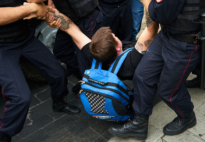 Man with blue backpack being detained by officers in a parking lot representing ICE intervention and foreign language issue. Man with blue backpack being detained by officers in a parking lot representing ICE intervention and foreign language issue.