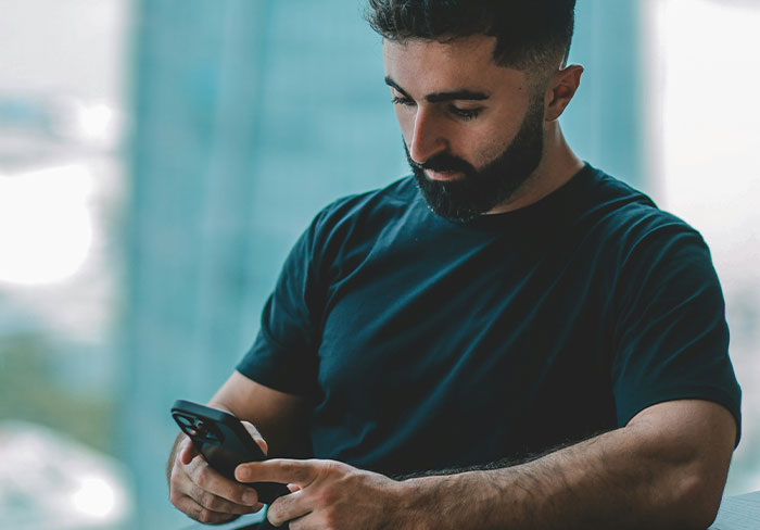 Man with beard using smartphone, representing ICE detainment and foreign language interaction themes in a parking lot setting. Man with beard using smartphone, representing ICE detainment and foreign language interaction themes in a parking lot setting.