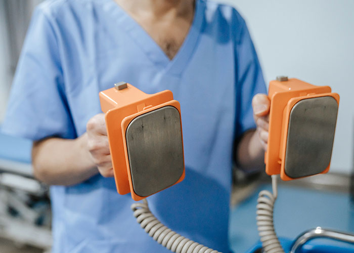 Person in medical scrubs holding old-fashioned defibrillator paddles illustrating fake facts from movies.