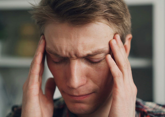 Young man with headache, holding temples, illustrating confusion about fake facts from movies and common misconceptions.