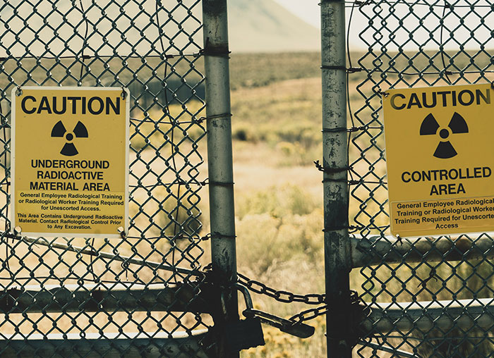 Caution signs on a locked chain-link fence warning of underground radioactive material and controlled area risks.