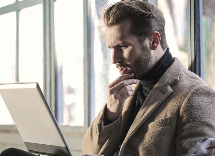 Man in a brown coat thoughtfully looking at laptop screen, illustrating fake facts people believed from movies.