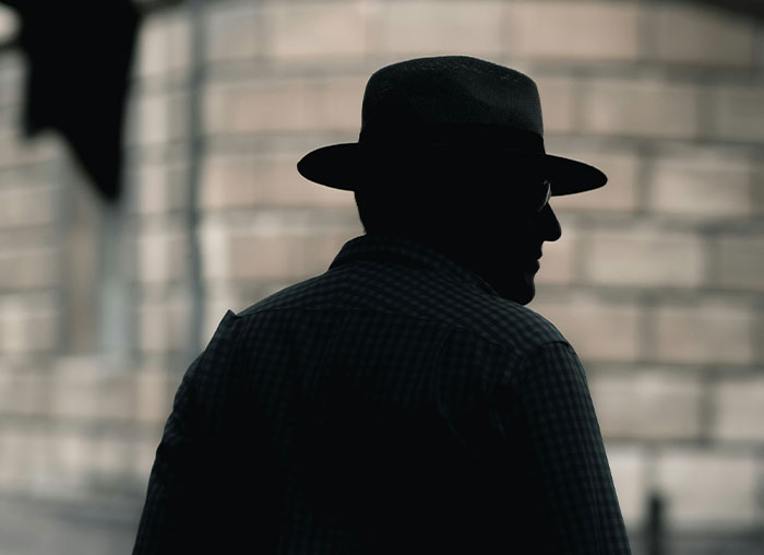 Silhouette of a man wearing a fedora hat and glasses against a blurred brick wall background representing fake facts from movies.